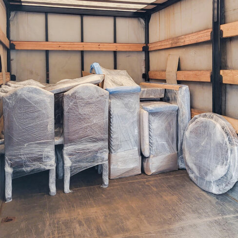 Mehrere sorgfältig mit Schutzfolie verpackte Möbelstücke stehen ordentlich gestapelt in einem Transportfahrzeug, bereit für den sicheren Umzug oder die Einlagerung.