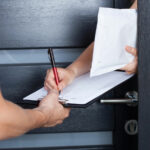 Eine Person unterschreibt auf einem Klemmbrett den Empfang eines Briefumschlags, der von einem Kurierdienst zugestellt wurde.