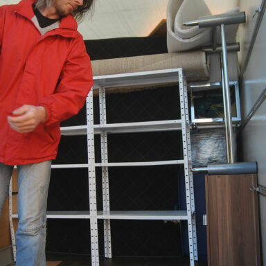 Eine Person steht in einem Transportfahrzeug und ordnet Möbelstücke sowie Regalteile für die Einlagerung oder den Transport.