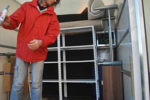 Eine Person steht in einem Transportfahrzeug und ordnet Möbelstücke sowie Regalteile für die Einlagerung oder den Transport.