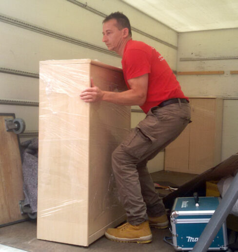 Eine Person mit weißen Handschuhen verpackt ein großes Möbelstück sorgfältig mit transparenter Schutzfolie, um es für den Transport zu sichern.